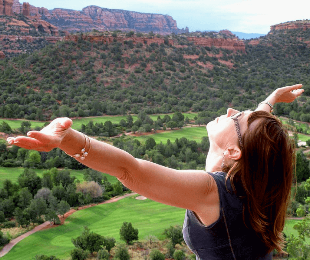 Woman raises her arms to the sun while overlooking the red rocks of Sedona