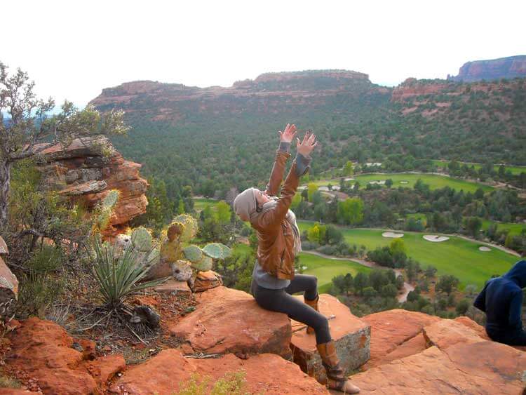 Woman seated on red rocks reaching to the sky.